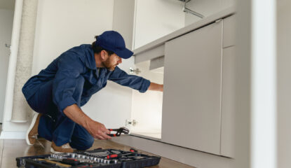 Professional plumber fixing broken water tap in residential kitchen.